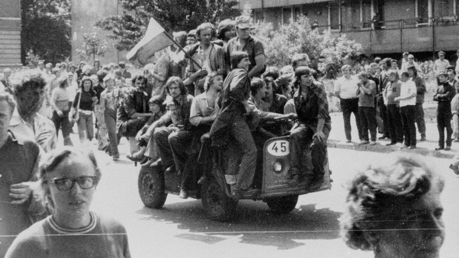 Radomski czerwiec '76. Grupa młodych ludzi jadących akumulatorowym wózkiem z narodową flagą pod gmach Komitetu Wojewódzkiego PZPR. Fot. PAP 