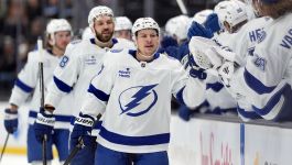 Na zdjęciu widzimy zawodników Tampa Bay Lightning, którzy w białych strojach z charakterystycznym błyskawicznym logotypem świętują kolejne zwycięstwo. Hokeiści przybijają sobie piątki na ławce rezerwowych, co podkreśla świetną atmosferę i pewność siebie, panujące w zespole po odniesieniu piątej wygranej z rzędu w rozgrywkach NHL. Kluczowe miejsce na pierwszym planie zajmuje zawodnik Lightning, który po udanej akcji otrzymuje gratulacje od kolegów, obrazując dynamikę i zespołowy charakter tej drużyny.