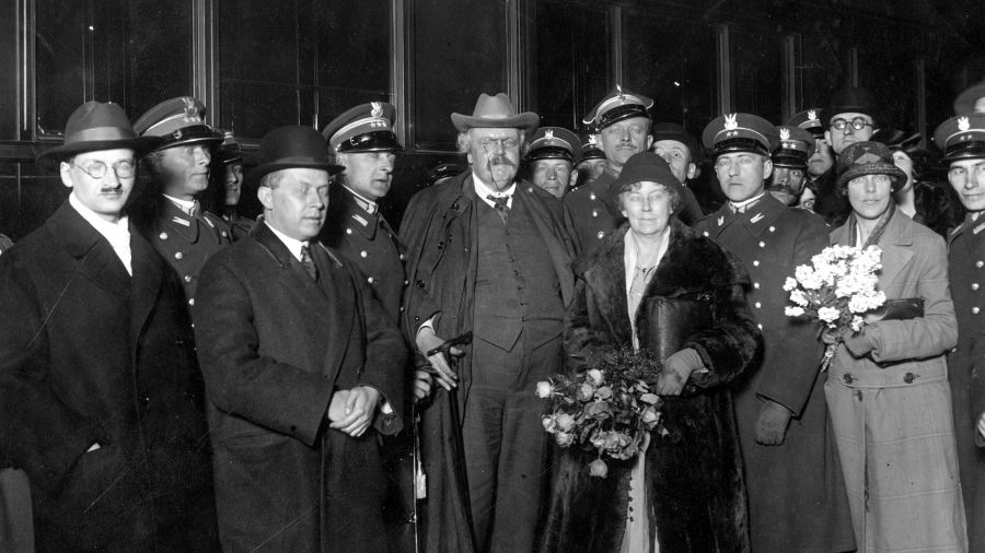 Wizyta Gilberta Keitha Chestertona (w środku, w kapeluszu) w kwietniu 1927 r. w Warszawie. Na dworcu witali go m.in. Wacław Borowy (1. z lewej), na prawo za nim rtm. Wacław Calewski, Ferdynand Goetel (2. z lewej) i za nim, też na prawo pułkownik Bolesław Wieniawa-Długoszowski. Na prawo od Chestertona major Adam Grocholski (z wąsami), adiutant ministra spraw wojskowych Józefa Piłsudskiego, a w głębi, w okularach Jan Lechoń. Fot. NAC/IKC, sygn. 1-K-2079-1