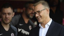 Na zdjęciu Daniel Kretinsky ubrany w białą koszulę i ciemną marynarkę. Obok stoją piłkarze Sparty.