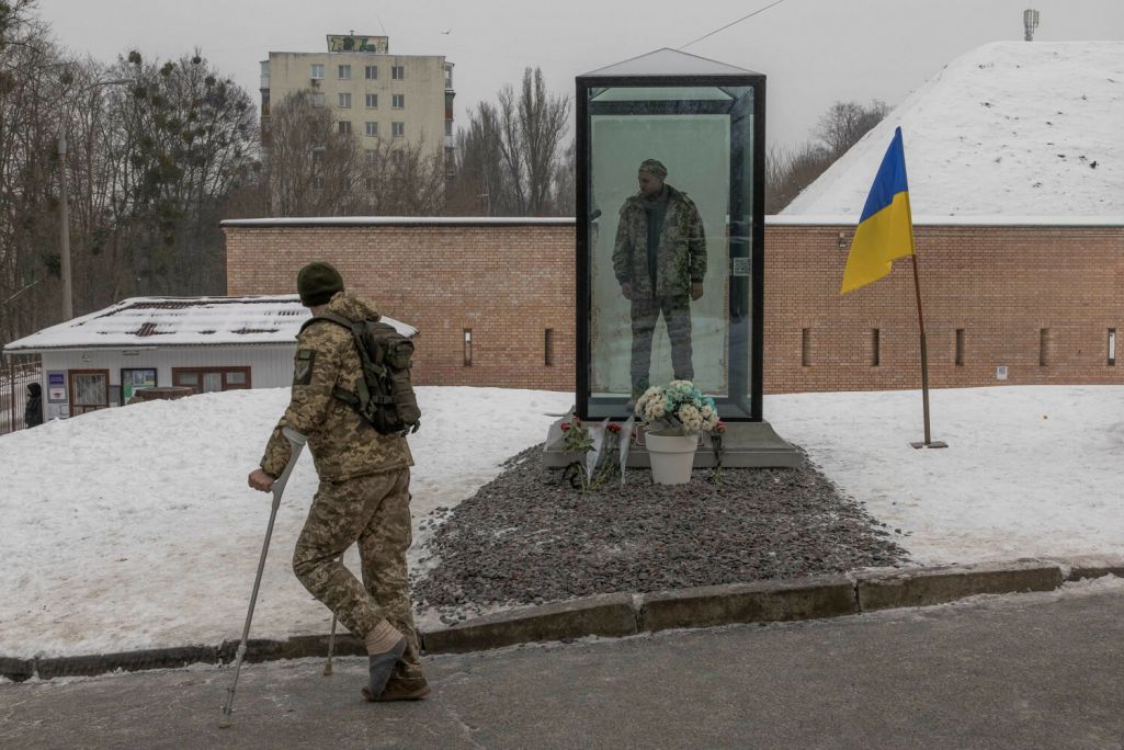 Вайсковец на мыліцах глядзіць на мемарыяльны помнік, нядаўна пастаўлены ў гонар загінулага ўкраінскага салдата Аляксандра Маціеўскага, у Кіеве. Пры канцы снежня 2022 года расейскія жаўнеры расстралялі Аляксандра Маціеўскага за словы «Слава Украіне» і выклалі гэтае відэа ў інтэрнэт. Кіеў, Украіна. 7 снежня 2023 года. (Фота: Roman Pilipey / AFP / East News)