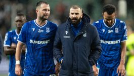 Zawodnicy Lecha Poznań (fot. Getty Images) Na zdjęciu widzimy zawodników Lecha Poznań tuż po zakończeniu jednego z meczów 14. kolejki Ekstraklasy. Ubrani w niebieskie stroje z logo sponsora "SUPERBET", stoją na murawie w wyraźnie zamyślonym nastroju. W centrum kadru znajduje się członek sztabu szkoleniowego w granatowej kurtce, który zdaje się prowadzić krótką rozmowę z piłkarzami (fot. Getty Images)