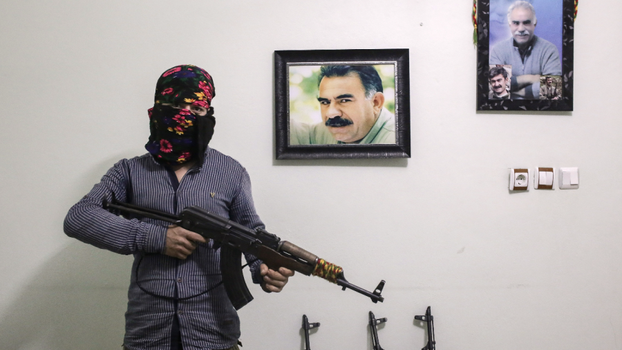Kurdyjski bojownik pozuje z AK-47, na ścianie wiszą obrazy z wizerunkiem uwięzionego lidera PKK  Abdullaha Ocalana (Fot.: Cagdas Erdogan/Getty Images).