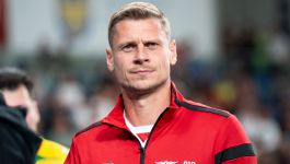 Łukasz Piszczek (fot. Getty Images) Były piłkarz w czerwonej sportowej kurtce z czarnymi wstawkami i widocznym logo GKS Tychy, stojący w hali lub na stadionie podczas oficjalnej prezentacji jako nowy trener drużyny. W tle rozmyte postacie i elementy trybun